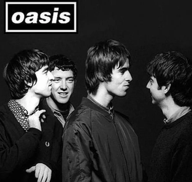 Capa do álbum 'Definitely Maybe' da banda Oasis. A foto em preto e branco mostra quatro jovens membros da banda interagindo entre si contra um fundo preto, com o logotipo 'Oasis' no canto superior esquerdo.