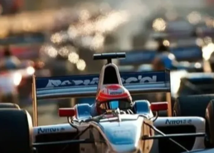 Um carro de corrida estilo Fórmula 1, nas cores branco e azul, visto de frente em primeiro plano e em foco nítido. Ele está em uma pista, e ao fundo, outros carros de corrida aparecem desfocados sob uma luz quente de fim de tarde.