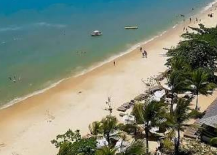 Vista aérea da praia em frente ao La Torre Resort All Inclusive em Porto Seguro, mostrando o mar em tons de azul e verde, faixa de areia clara, coqueiros e a estrutura de sombreiros brancos do resort à beira-mar.